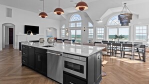 A spacious kitchen with a large island, modern pendant lights, and a view of the ocean through large windows. - 2876 - The Blue Martini - Oceanfront Luxury Retreat w/ Pool & Sauna (Duck)