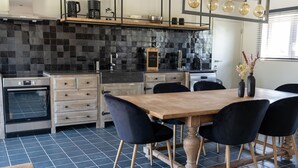 Una cocina moderna con salpicadero de baldosas negras, armarios de madera, horno empotrado y comedor con mesa de madera y sillas negras.