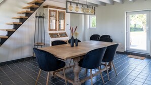 Un comedor con una mesa de madera, sillas azul oscuro, una escalera con escalones de madera y un suelo de baldosas negras.