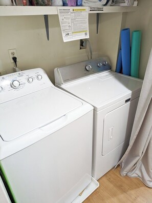 A laundry area with two washing machines, a power outlet, and a wall-mounted instruction guide.