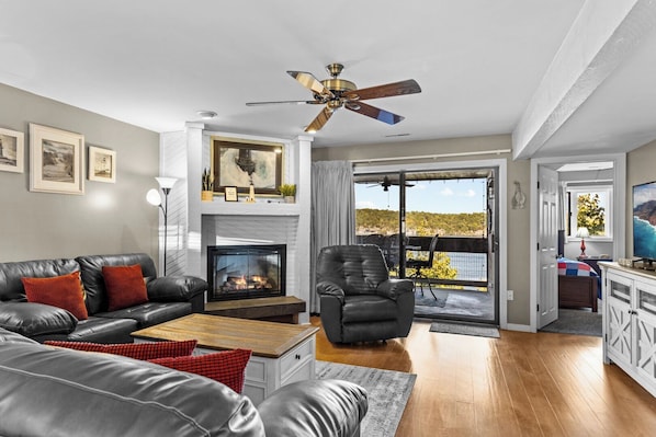 A living room with a fireplace, leather sofa, and a view of a natural landscape.