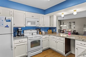 A kitchen with white cabinets, a microwave, a stove, and a coffee maker.
