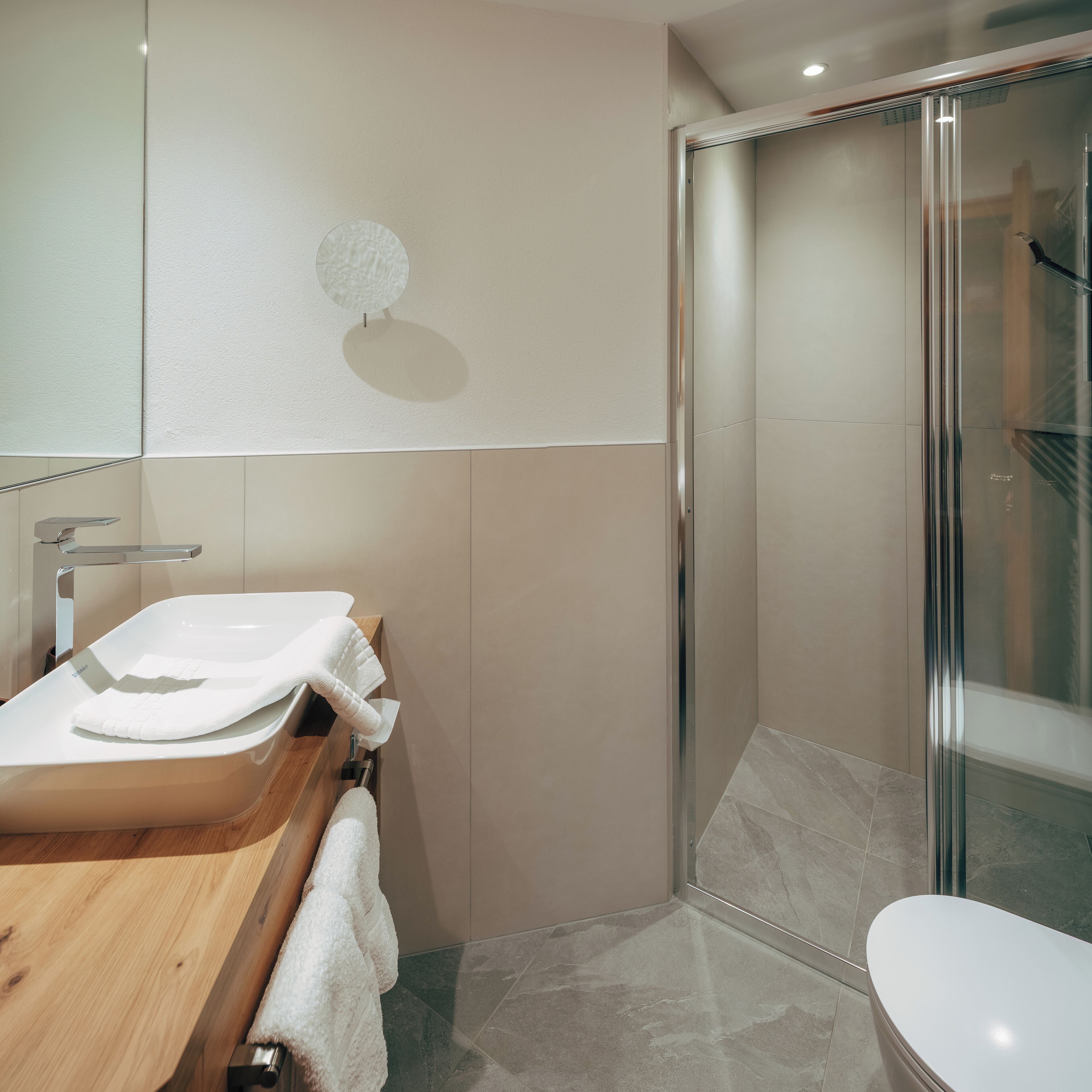 A modern bathroom with a wooden vanity, a glass shower enclosure, and a toilet.