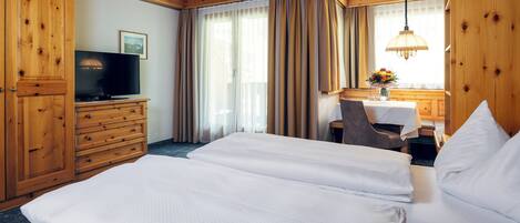 Habitación de hotel con dos camas, muebles de madera, televisor y ventana con cortinas.
