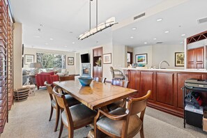 A spacious dining area with a wooden table and chairs, a kitchen with wooden cabinets, and a large window providing natural light.