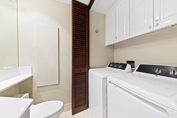 A laundry room with a washing machine and dryer, a toilet, and a cabinet above the dryer.