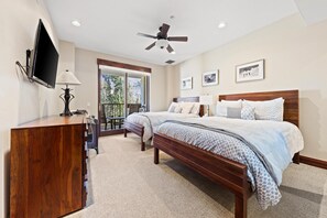 A bedroom with a bed, a desk, a chair, a ceiling fan, and a TV mounted on the wall.
