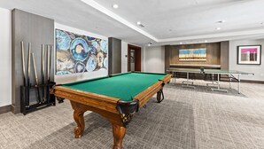Een pooltafel in een ruimte met een tapijtvloer, een muur met abstracte kunst, en een tafeltennistafel op de achtergrond.