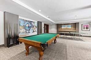 Een pooltafel in een ruimte met een tapijtvloer, een muur met abstracte kunst, en een tafeltennistafel op de achtergrond.