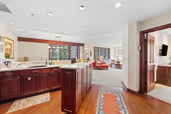 A spacious kitchen with a large island, wooden cabinets, and a view of the living area.