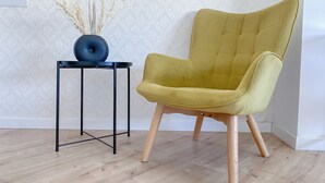A yellow armchair with wooden legs and a black metal table with a vase of dried plants. - Phaedrus Living Plateia Suite Grigio (Nicosia)