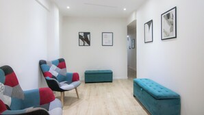 A modern waiting area with a wooden floor, a teal bench, and colorful chairs. - Phaedrus Living Plateia Suite Grigio (Nicosia)