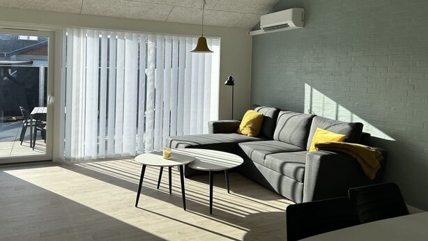 A modern living room with a grey sofa, two small tables, and a large sliding glass door leading to an outdoor area.