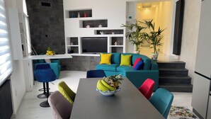 Una sala moderna con una mesa de comedor negra, sillas coloridas, un sofá color turquesa con cojines y un televisor montado en la pared.