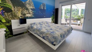 Un dormitorio con cama, televisor, ventana grande y vista al mar.