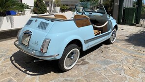 Un coche descapotable azul celeste antiguo estacionado sobre un pavimento de piedra.