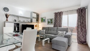 Ein modernes Wohnzimmer mit einem Glastisch, einer grauen Couch, weißen Stühlen und einem Essbereich mit einem Glastisch.