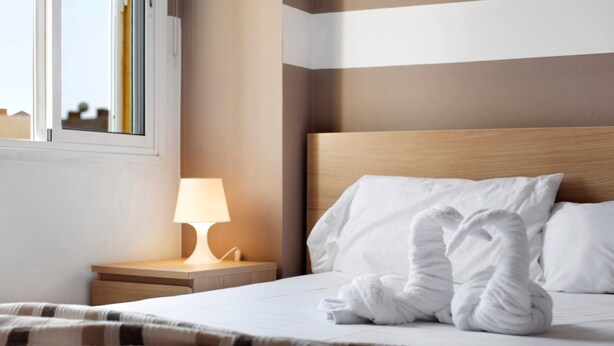 Ein Hotelzimmer mit Bett, Nachttisch mit Lampe und Fenster.