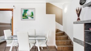 Ein Essbereich mit Glastisch und weißen Stühlen, eine Treppe mit Holzstufen, ein gerahmtes Gemälde und eine Uhr an der Wand.