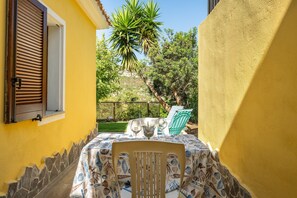 Un patio con una mesa preparada para dos, una silla y vistas a un jardín y árboles.