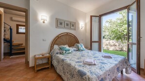 Une chambre à coucher comprenant un lit, des tables de chevet, une commode, une fenêtre donnant sur un espace verdoyant et un escalier menant à un autre niveau.