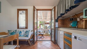 Une cuisine compacte équipée d’un lave-vaisselle, un coin repas avec un banc et des chaises, et une vue sur une terrasse extérieure.