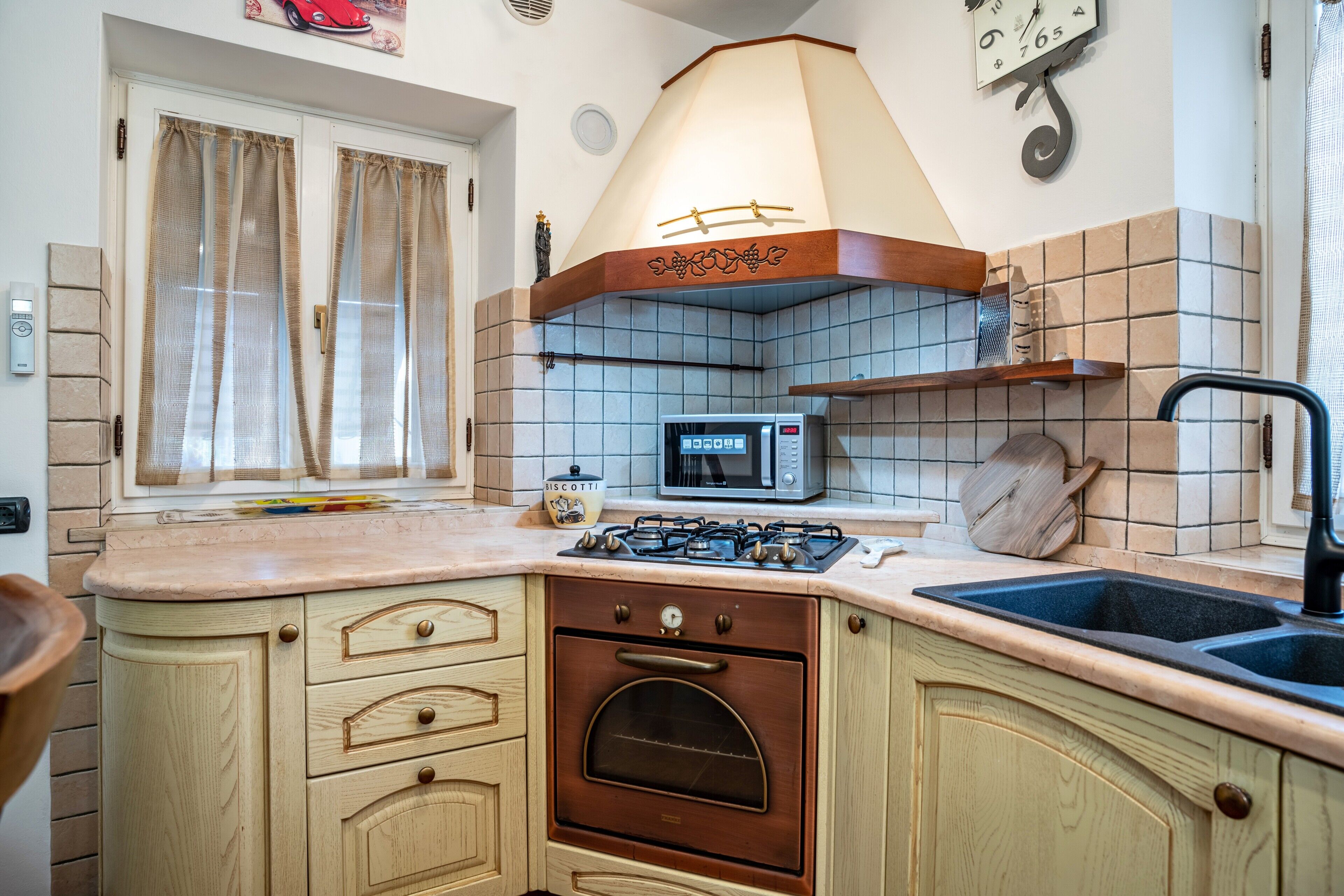 A kitchen with a stove, oven, microwave, sink, and window with curtains.