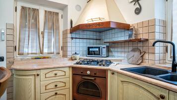 A kitchen with a stove, oven, microwave, sink, and window with curtains.
