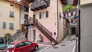 Une rue étroite où est garée une voiture rouge, un immeuble à la façade rose et un escalier menant à un étage supérieur.