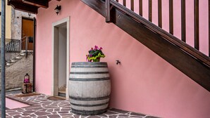 Un bâtiment aux murs de couleur rose, avec une entrée carrelée en pierre, un grand tonneau et un escalier en bois.