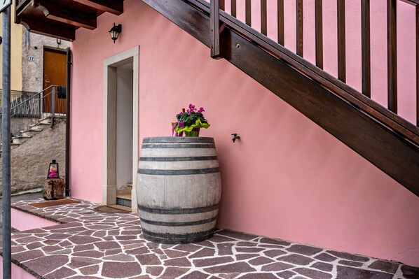 Un bâtiment aux murs de couleur rose, avec une entrée carrelée en pierre, un grand tonneau et un escalier en bois.
