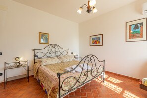 A bedroom with a metal bed frame, floral bedding, a chandelier, and two framed artworks on the walls.