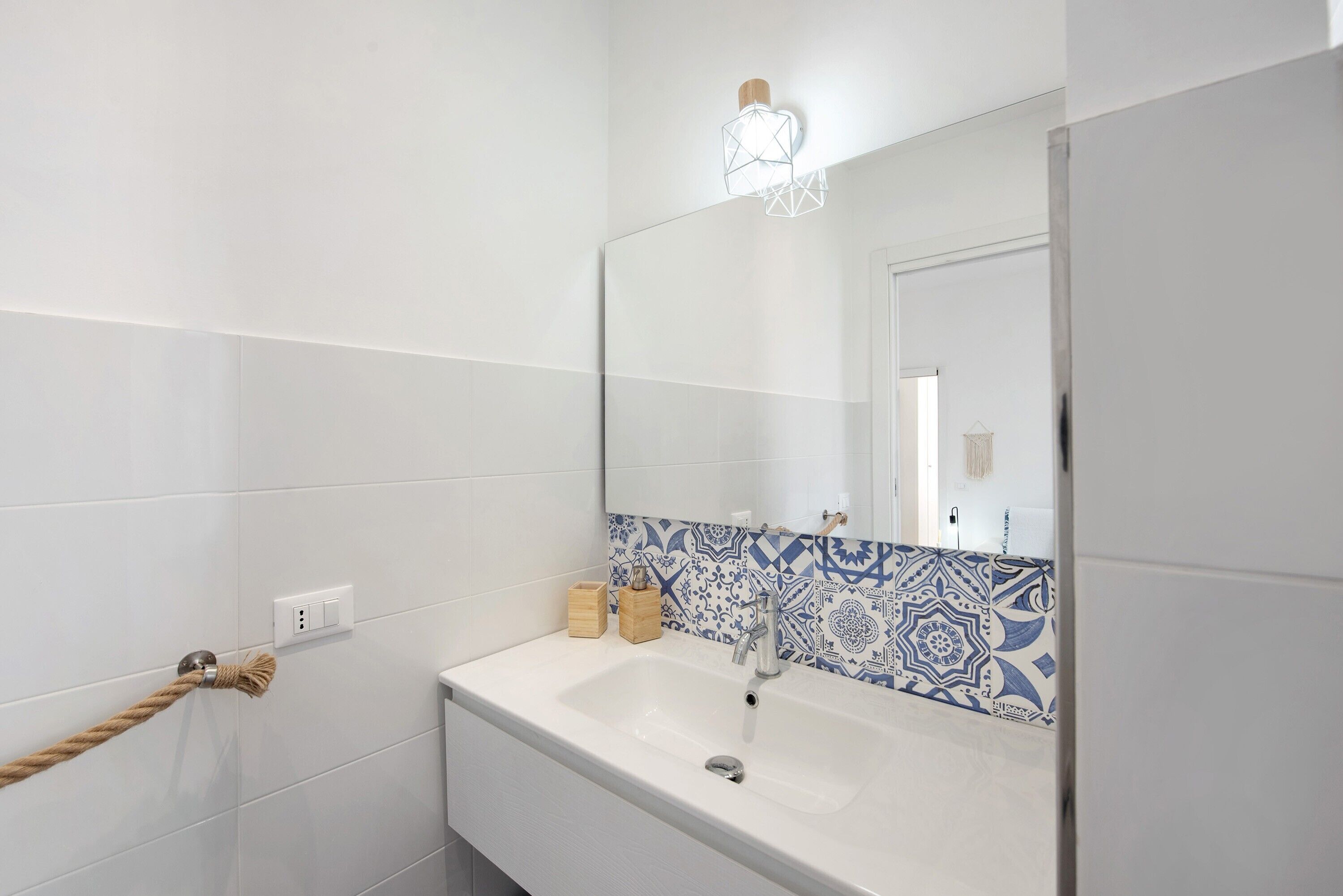 A bathroom with white tiles, a blue patterned backsplash, a white sink, a mirror, and a towel rack.