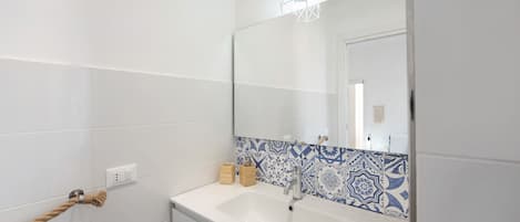 A bathroom with white tiles, a blue patterned backsplash, a white sink, a mirror, and a towel rack.