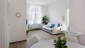 A modern living room with a white sofa, a dining table, and a plant. - Rosa Corallo Deluxe – Historic Center Apartment with Wi-Fi and Air Conditioning (Varazze)