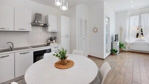 A modern kitchen with white cabinets, a round dining table, and pendant lighting. - Rosa Corallo Deluxe – Historic Center Apartment with Wi-Fi and Air Conditioning (Varazze)