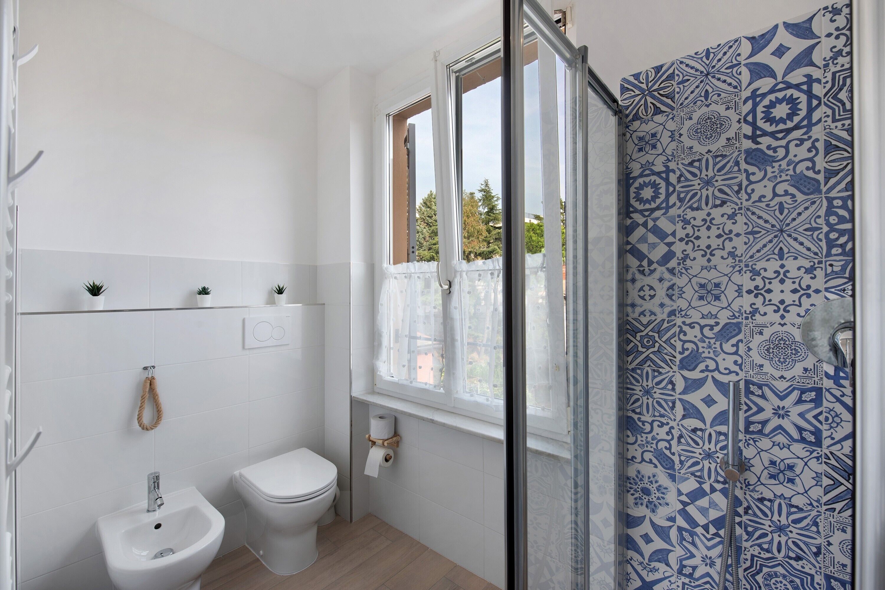 Ein Badezimmer mit integriertem Bidet, Toilette und einem Fenster mit Blick auf Bäume.