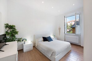 Ein Schlafzimmer mit Bett, Nachttischen, Schreibtisch, Pflanze und Fenster mit Blick.