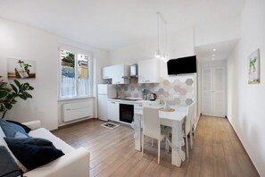 A modern kitchen with white cabinets, a dining area with a white table and chairs, and a large window.