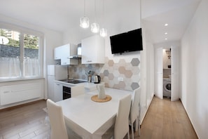 A modern kitchen with white cabinets, a flat-screen TV, and a dining area with a table and chairs.