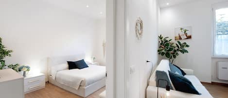 A modern bedroom with a bed, bedside table, and a small seating area with a lamp.
