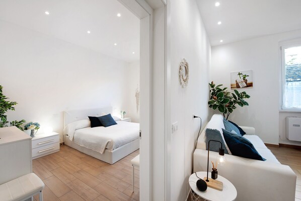 A modern bedroom with a bed, bedside table, and a small seating area with a lamp.