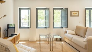 Un salon moderne avec un canapé, une table basse en verre et deux fenêtres ouvertes.
