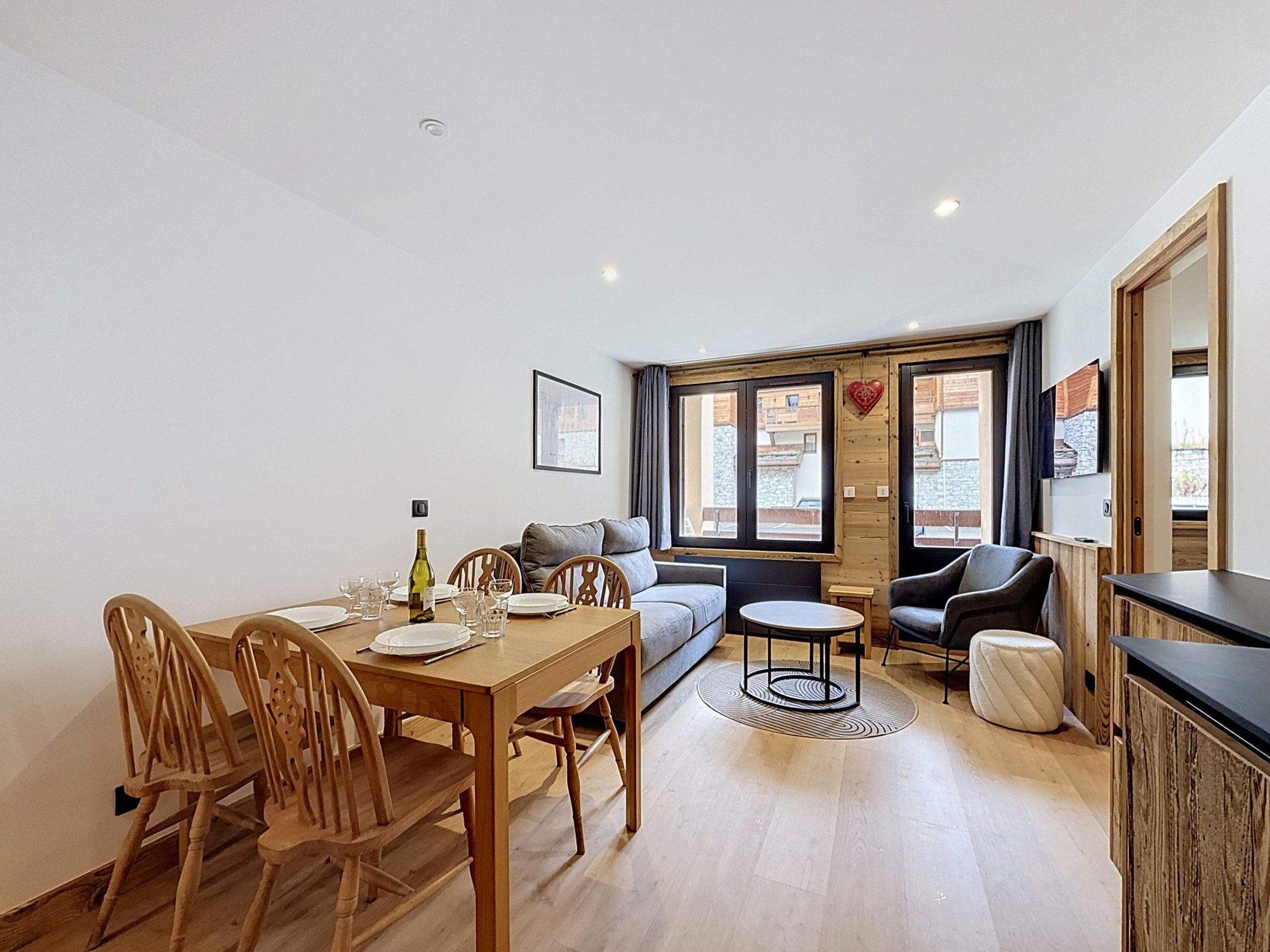 A dining area with a wooden table set for four, a sofa, a small round table, and a cabinet.