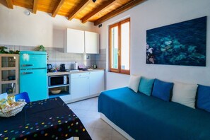 Una cocina compacta con un refrigerador turquesa, gabinetes blancos y una mesa de comedor con mantel de lunares.
