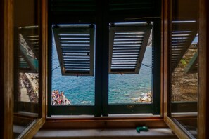 A window with shutters, overlooking a body of water and a rocky shoreline with people. - Casa Teresa with AC and Balcony  (Vernazza)