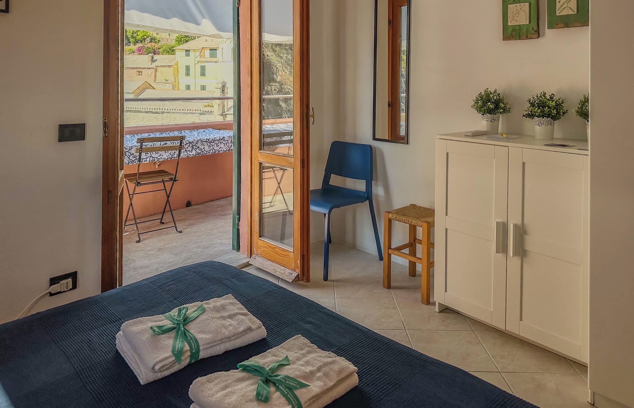 A hotel room with a bed, a chair, a small table, a cabinet, and a view of the outside.