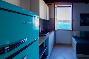 A compact kitchen with a teal refrigerator, a window offering a view of the sea, and a small seating area with a view. - Casa Teresa with AC and Balcony  (Vernazza)