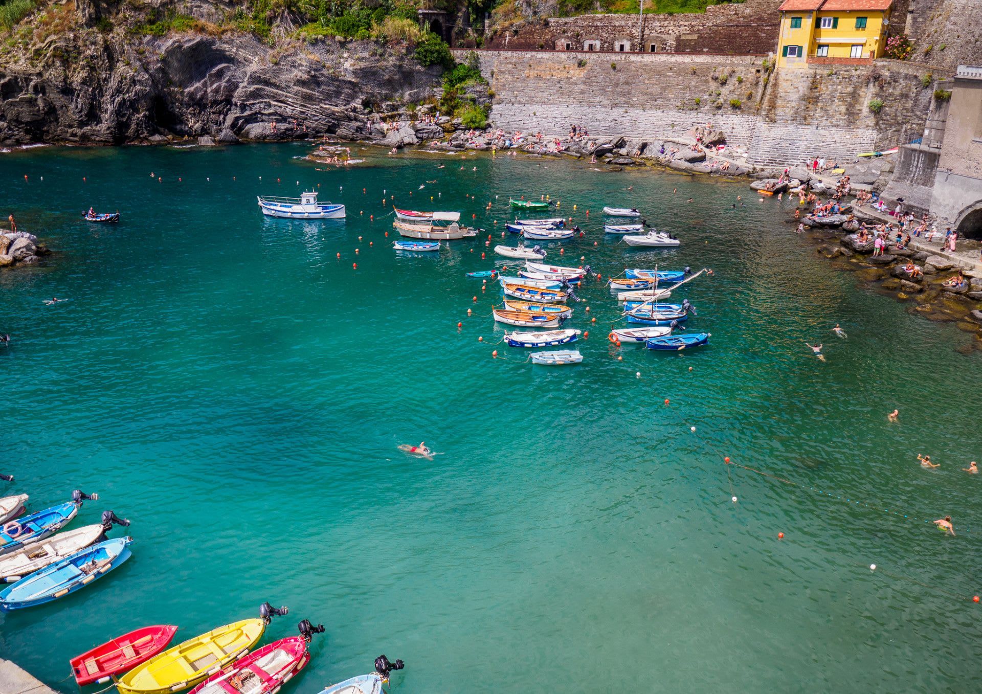 Cena costeira com barcos atracados e pessoas nadando na água.