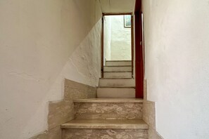 Un escalier étroit, avec une porte rouge en haut et une petite fenêtre en bas.